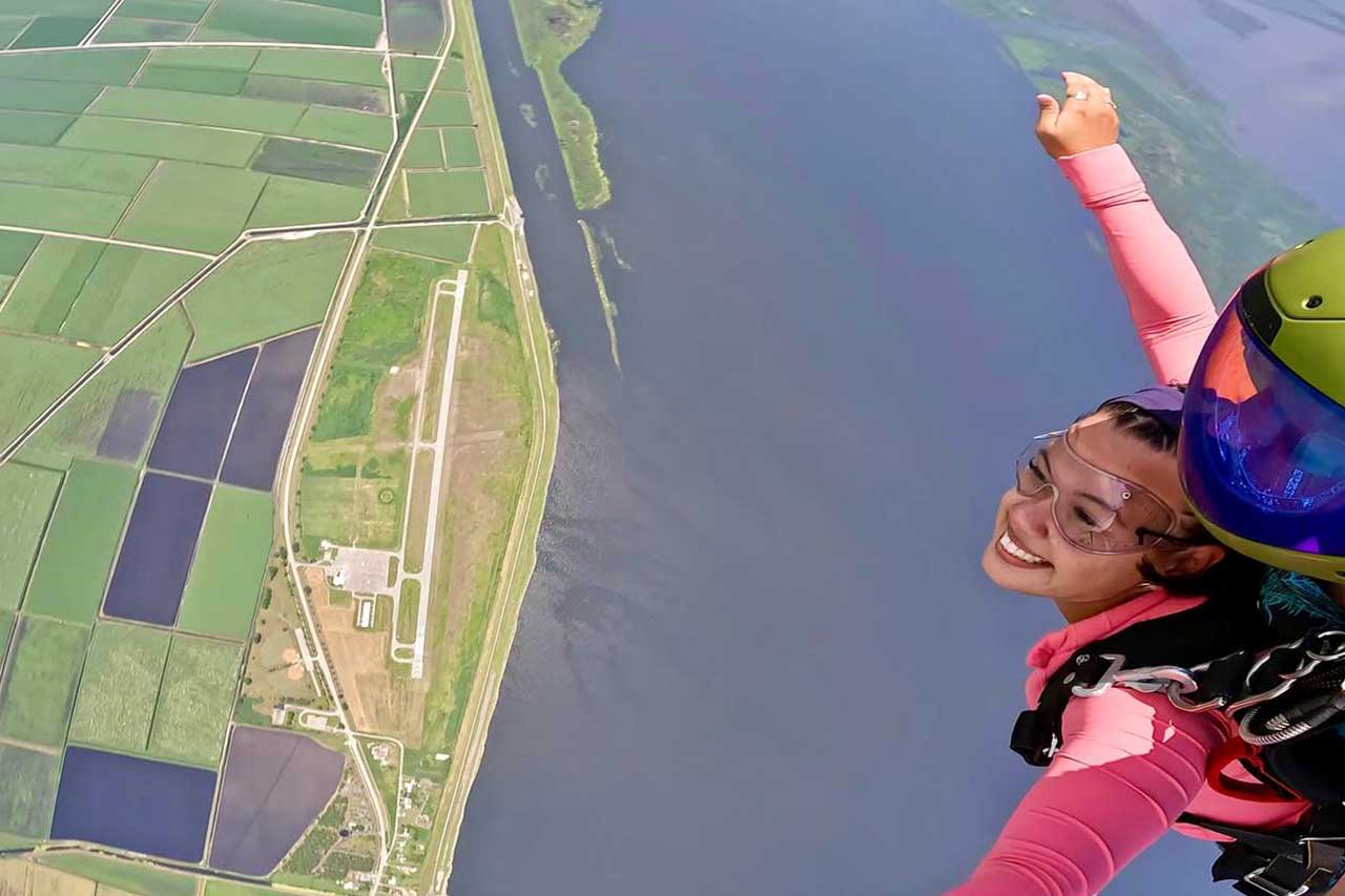 A girl in a pink jumpsuit on a tandem skydive smiling over the lake at Skydive Palm Beach