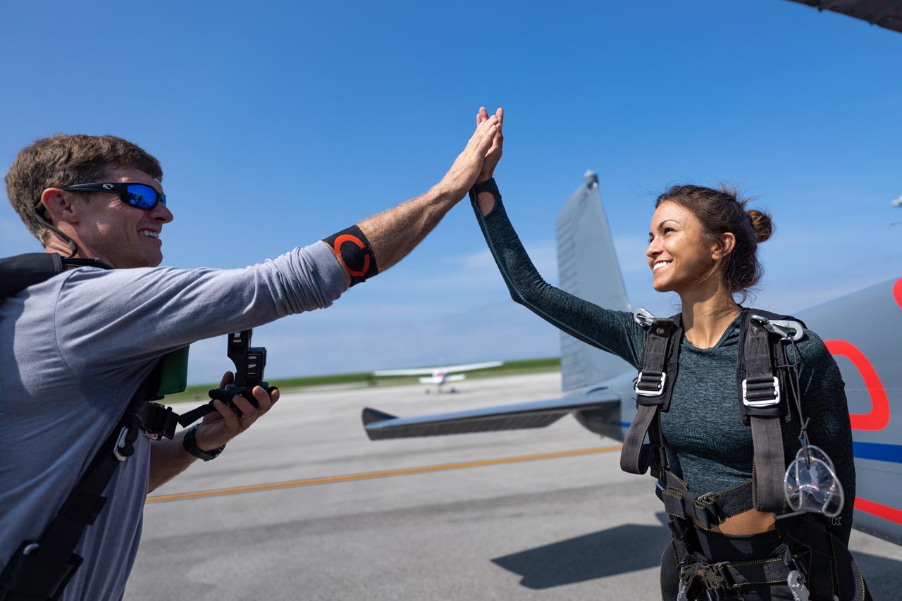 Tandem skydiving instructor gives a student a high five before boarding an airplane