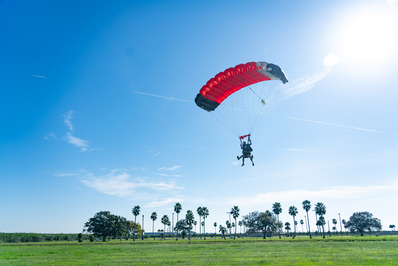 Tandem skydiving pair preparing to land in a grassy field at Skydive Palm Beach in South Florida