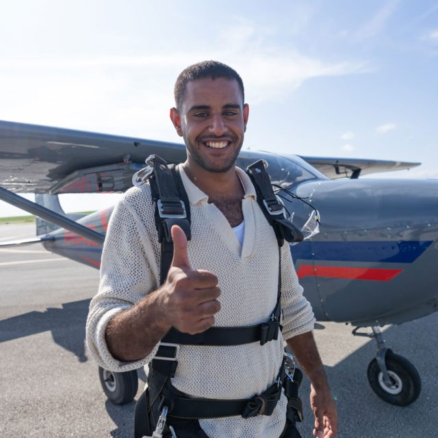 Male tandem skydiving student gives a thumbs up in front of an airplane at Skydive Palm Beach