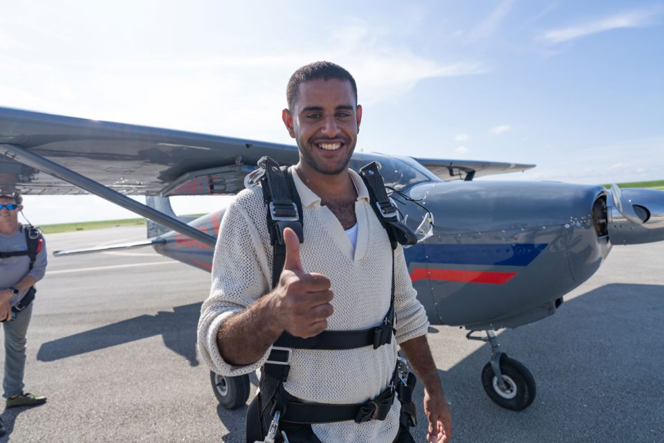 Male tandem skydiving student gives a thumbs up in front of an airplane at Skydive Palm Beach