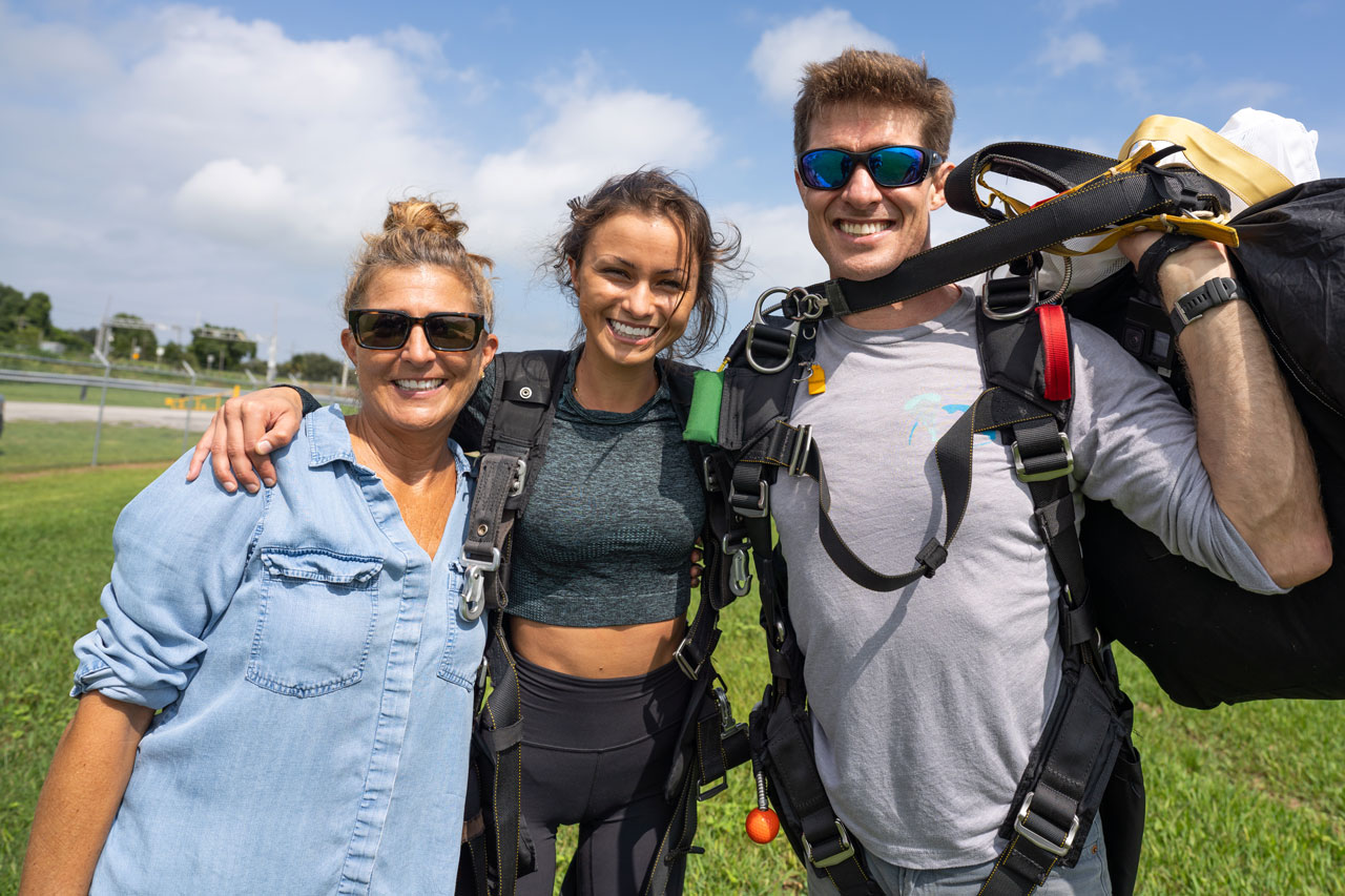 Tandem skydiving student and instructor pose for a photo with a family member after a skydive