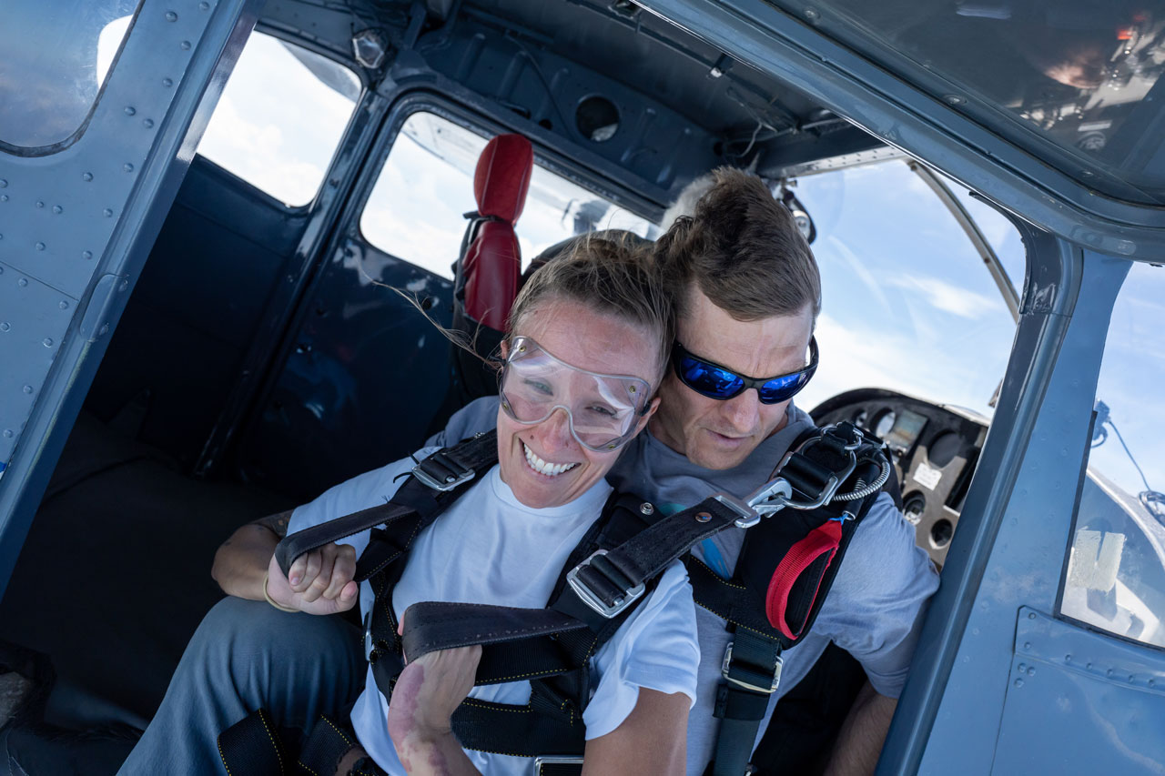 Tandem skydiving student and instructor sit in the door of an airplane preparing to jump