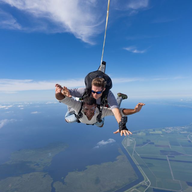 Male tandem skydiving student in white sweater in freefall above Lake Okeechobee in Florida.