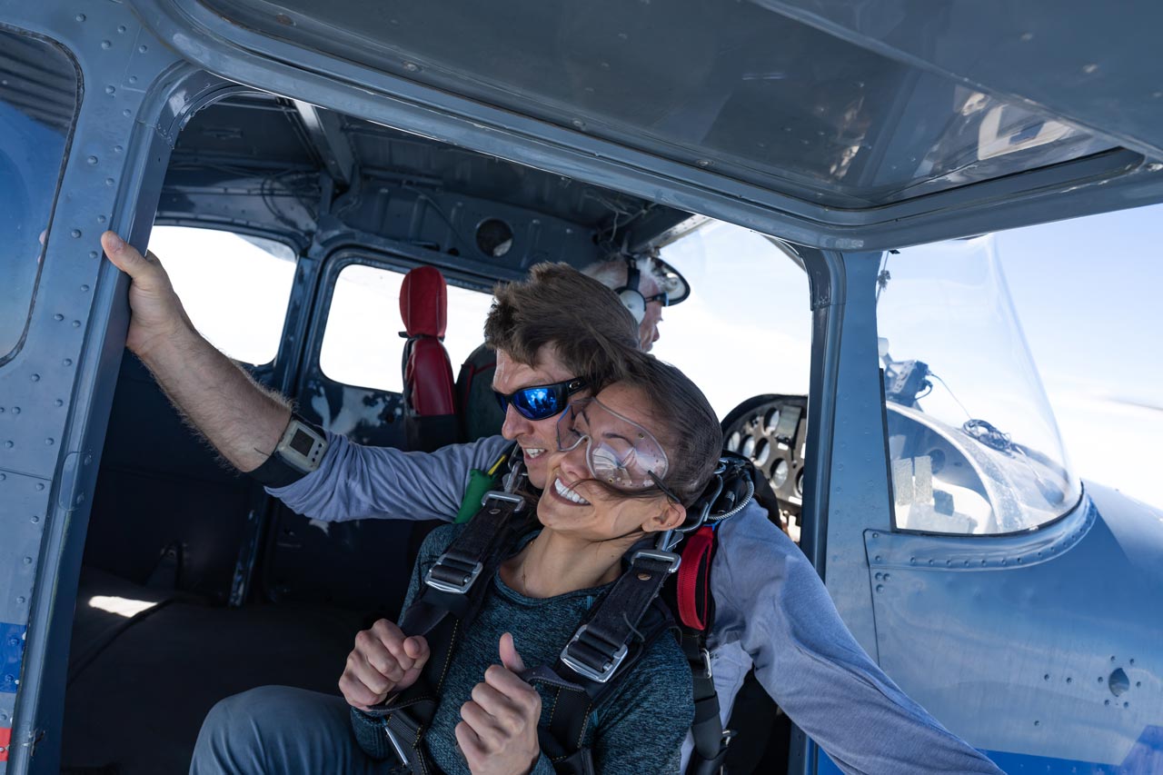 Tandem skydiving student and instructor sit in the door of an airplane preparing to jump