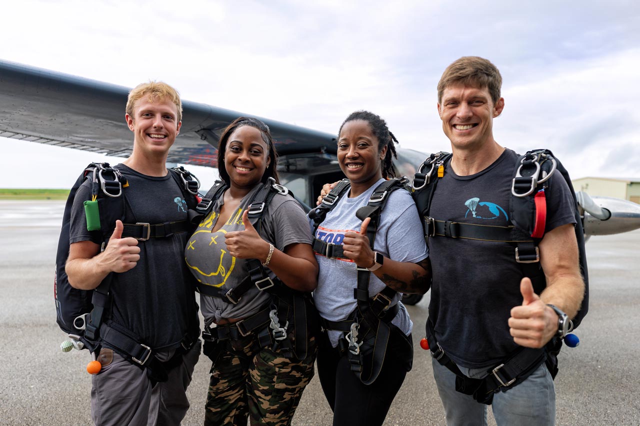 A group of tandem skydiving students and instructors smile in front an airplane at Skydive Palm Beach