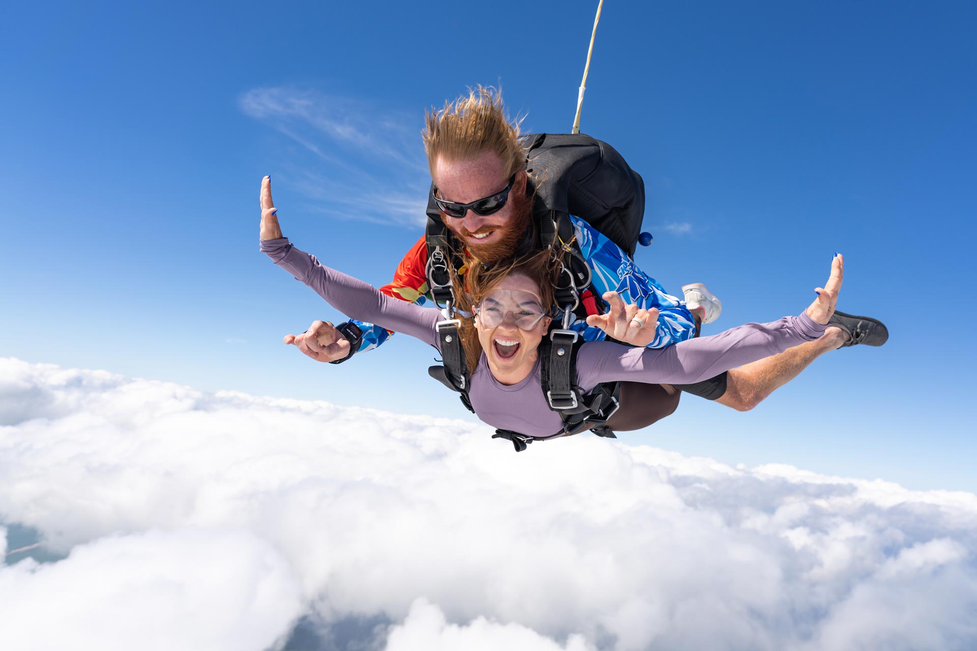 Female skydiving student in purple shirt smiles while in freefall during a tandem skydive