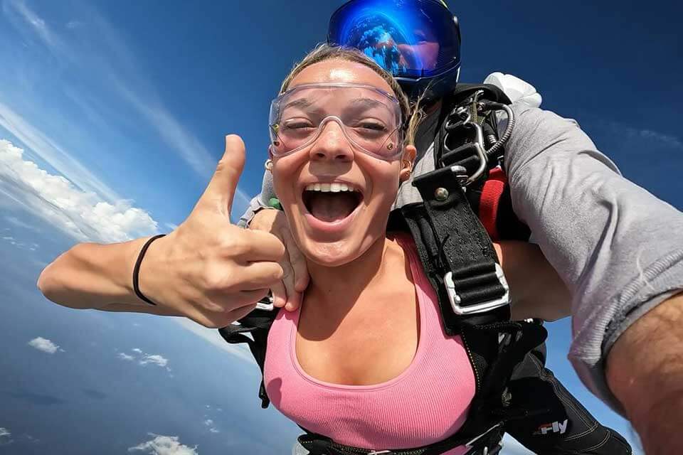 Female tandem skydiver in freefall gives a thumbs up