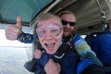 Smiling man with tandem skydiving instructor give thumbs up while preparing to exit the plane