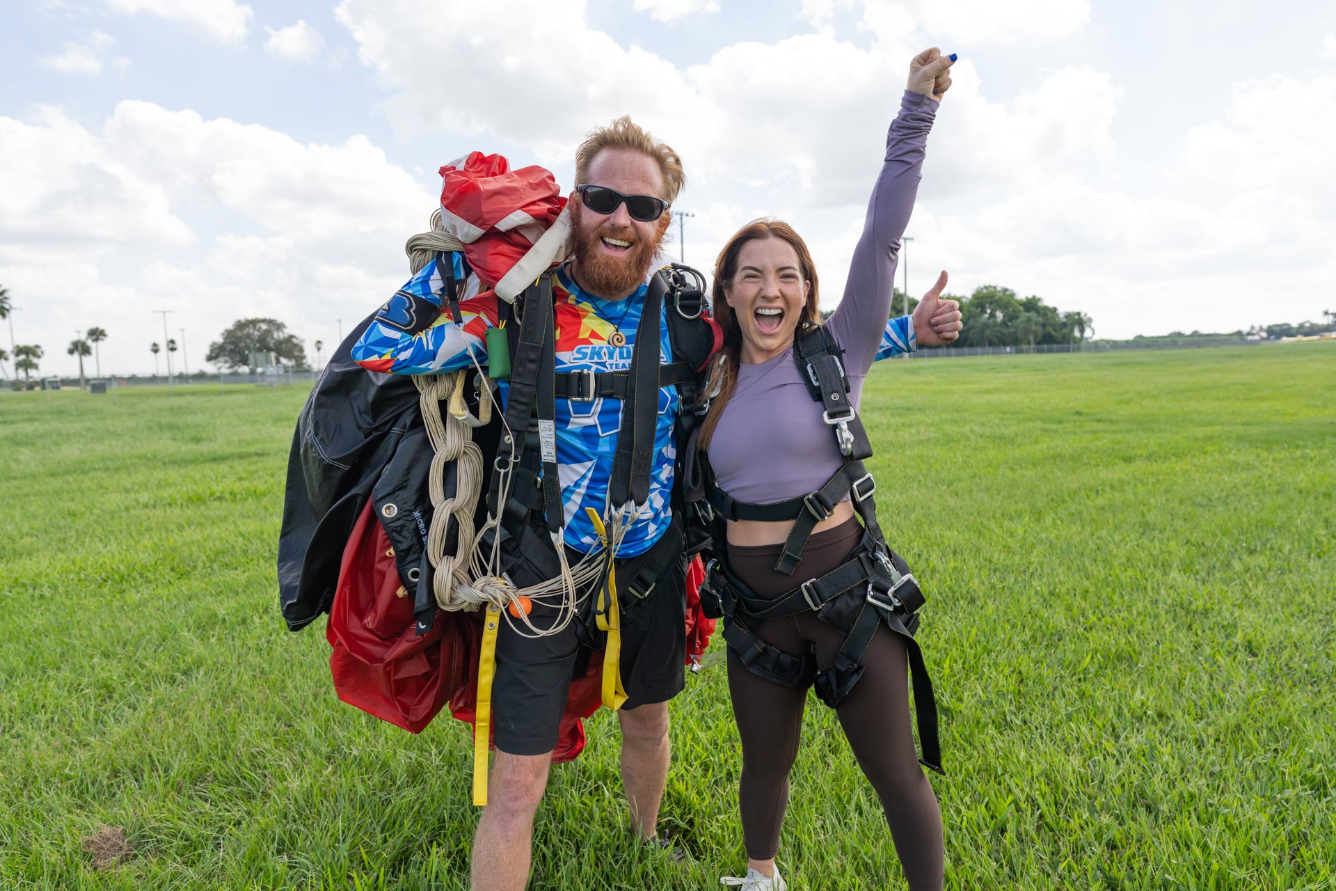 Female tandem skydiving student raises fist in the sky and smiles after landing from a skydive