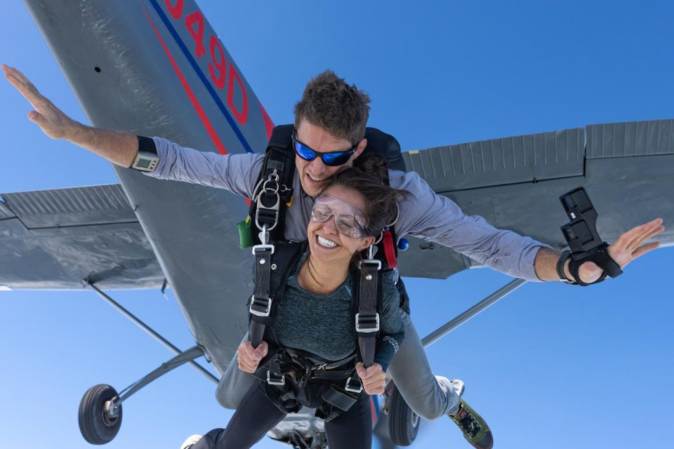 Tandem skydiving student and instructor exiting aircraft with plane and blue sky in background