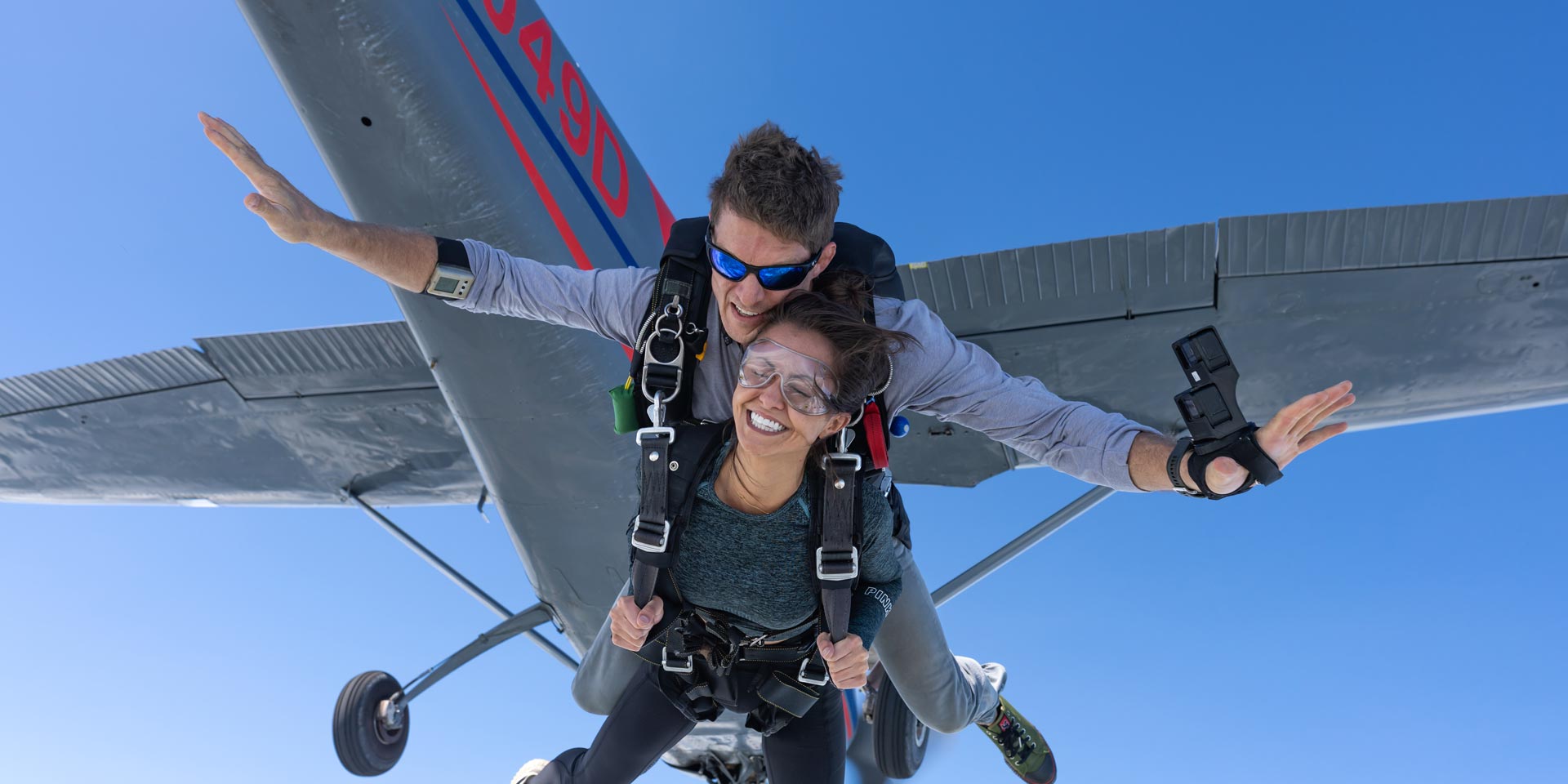 Tandem skydiving student and instructor exiting aircraft with plane and blue sky in background