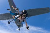 Tandem skydiving student and instructor exit plane with blue sky background