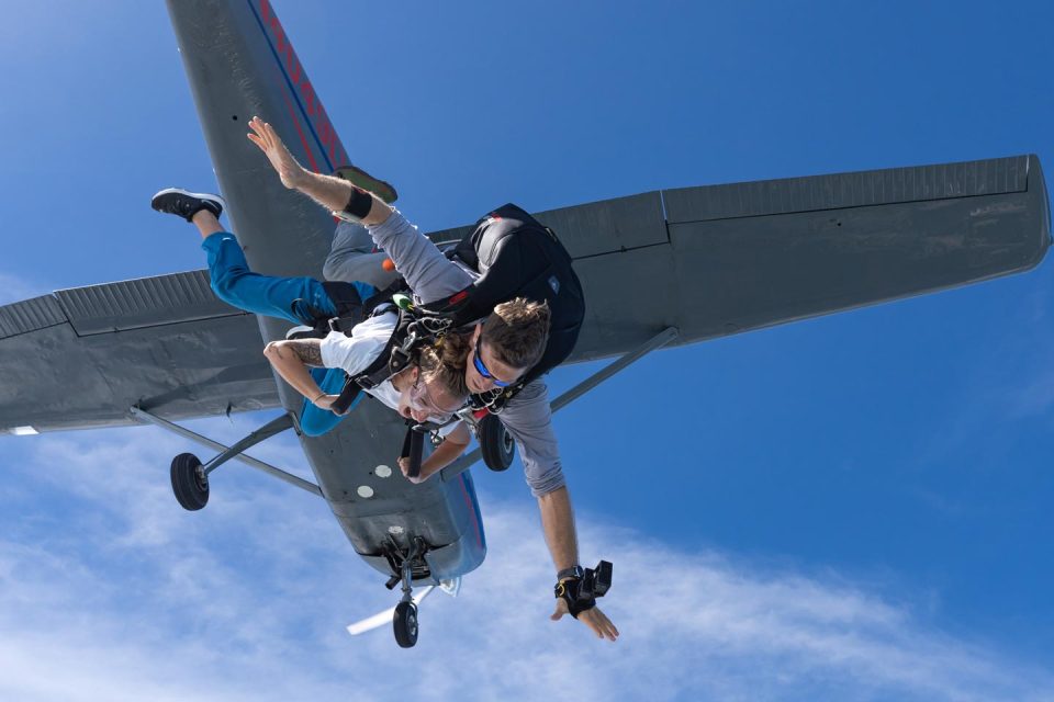 Tandem skydiving student and instructor exit plane with blue sky background