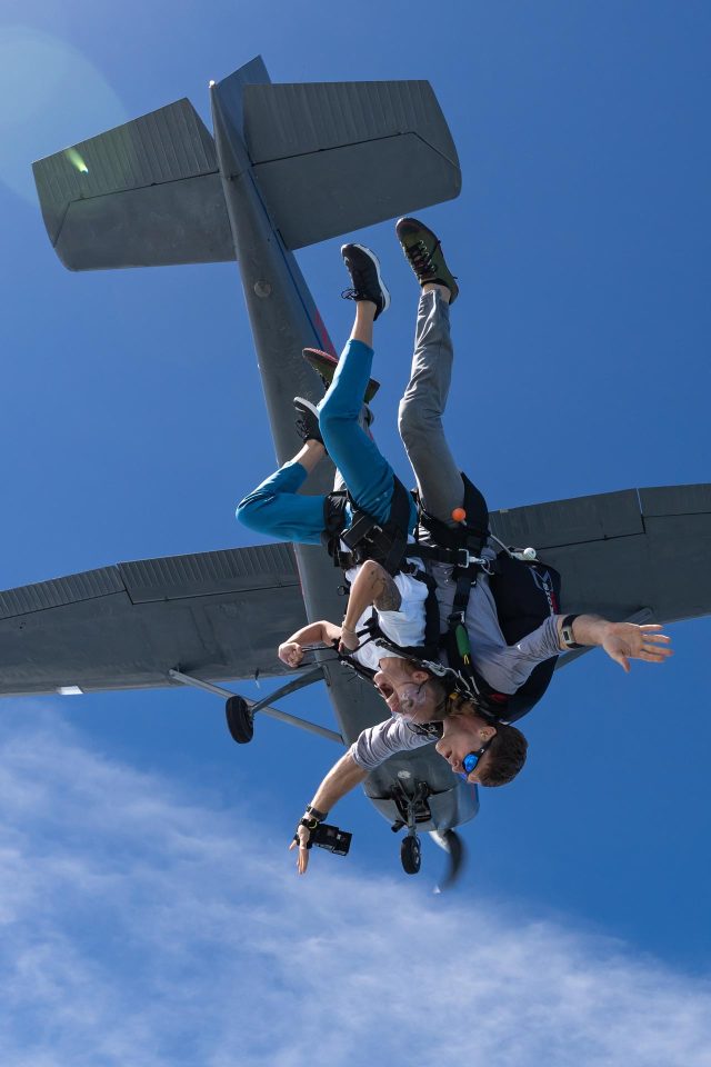 Tandem skydiving pair upside down in freefall with plane in background