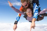 Female skydiving student in purple shirt smiles while in freefall during a tandem skydive