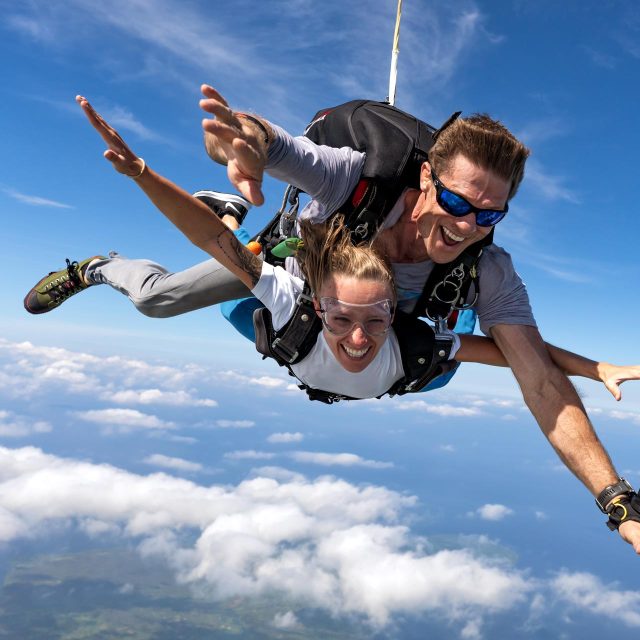 Female tandem skydiving student and male instructor in freefall with blue sky background