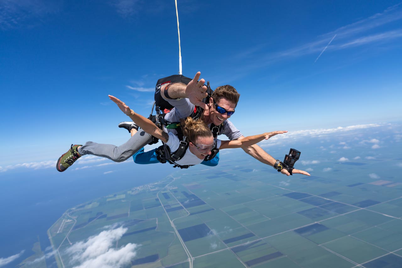 Female tandem skydiving student and male instructor in freefall with blue sky background