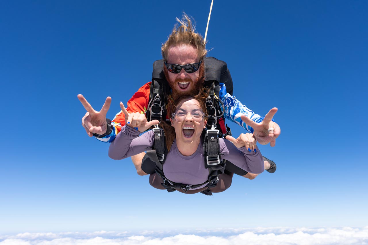 Tandem skydiving student gives the "rock on" hand signal while in freefall