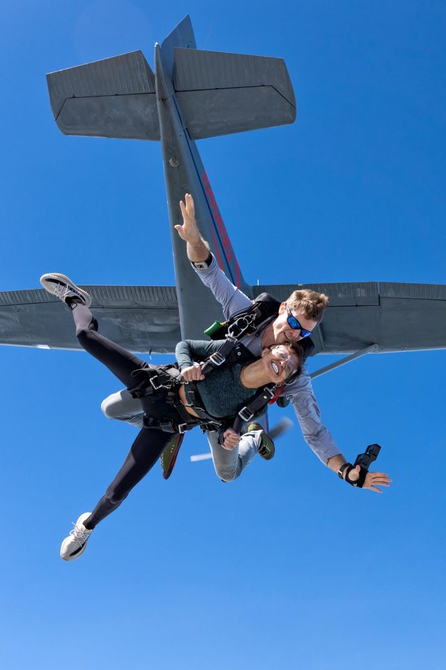 Tandem skydiving student and instructor exiting aircraft with plane and blue sky in background