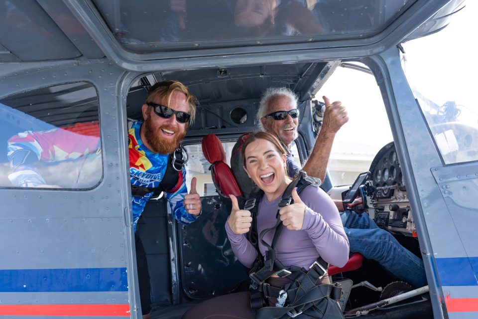 Tandem skydiving student, instructor, and pilot giving thumbs up in door of airplane at Skydive Palm Beach