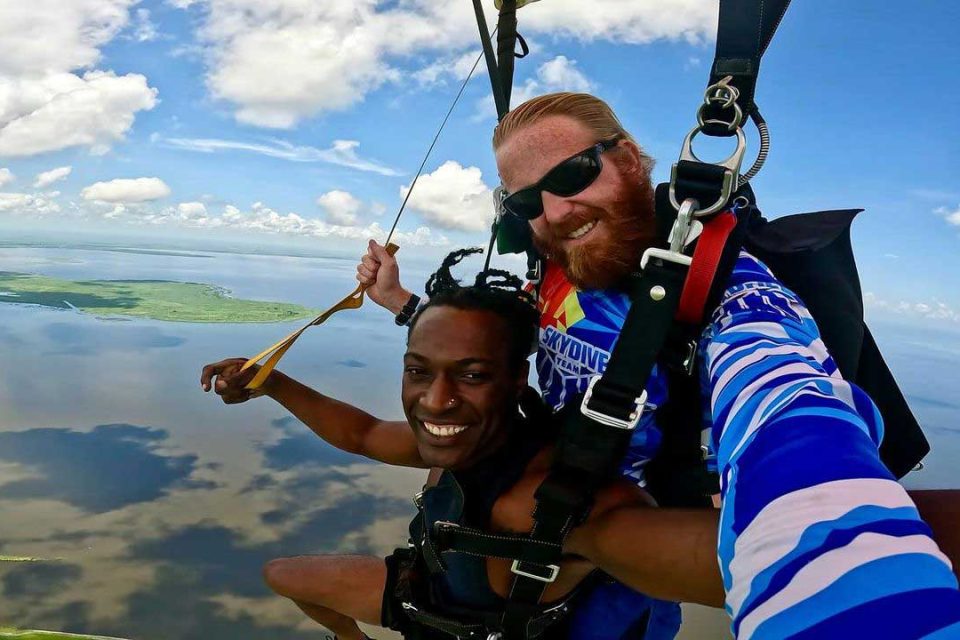 Man smiling under canopy with his instructor during a tandem skydive.