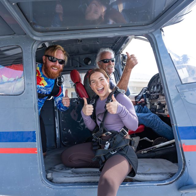 Tandem skydiving student, instructor, and pilot giving thumbs up in door of airplane at Skydive Palm Beach