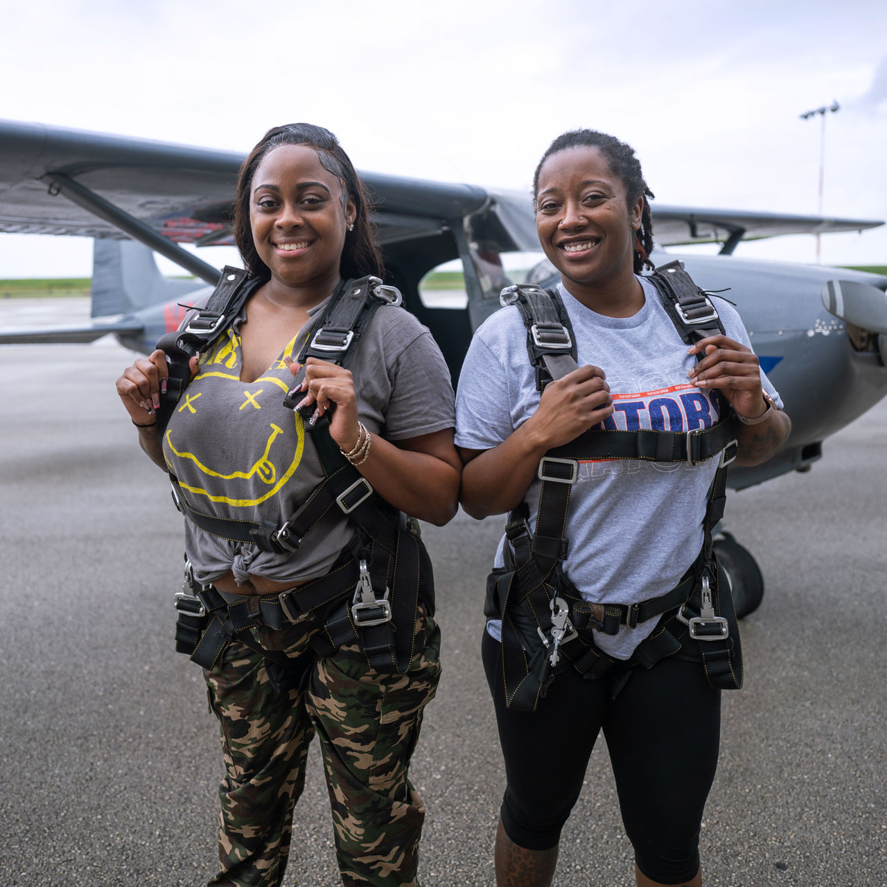 Two female tandem skydiving students pose in front of an airplane at Skydive Palm Beach in South Florida
