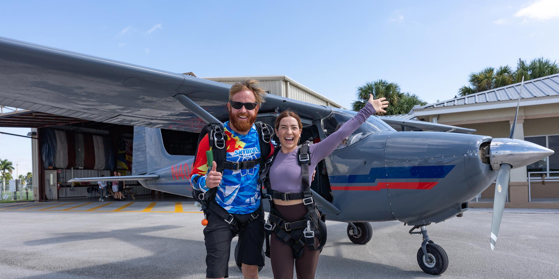 Tandem skydiving instructor and student smile for a photo in front of a skydiving plane at Skydive Palm Beach