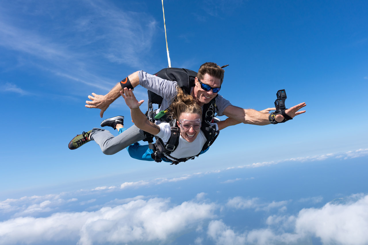 Female tandem skydiving student and male instructor in freefall with blue sky background