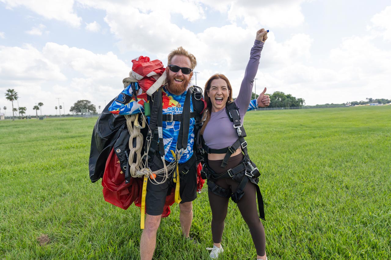 Female tandem skydiving student raises fist in the sky and smiles after landing from a skydive